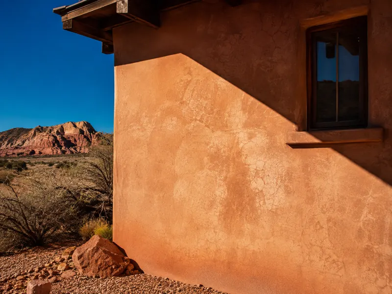Sun-beaten stucco wall with fine surface crazing beside red rock in Southern Utah