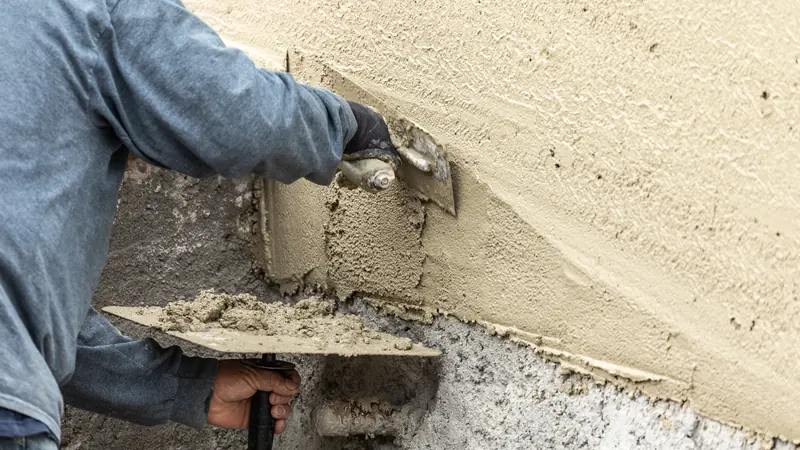 Plasterer applying a stucco coat with a hawk and trowel during a stucco installation