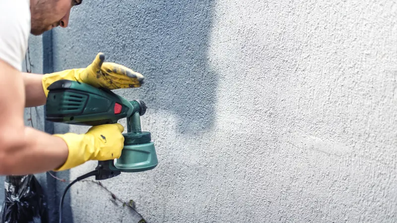 Sprayer applying a breathable coating over a textured stucco wall