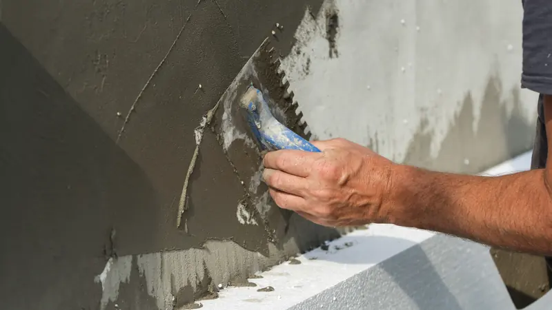 Mesh-reinforced base coat troweled over insulation board in an EIFS synthetic stucco assembly